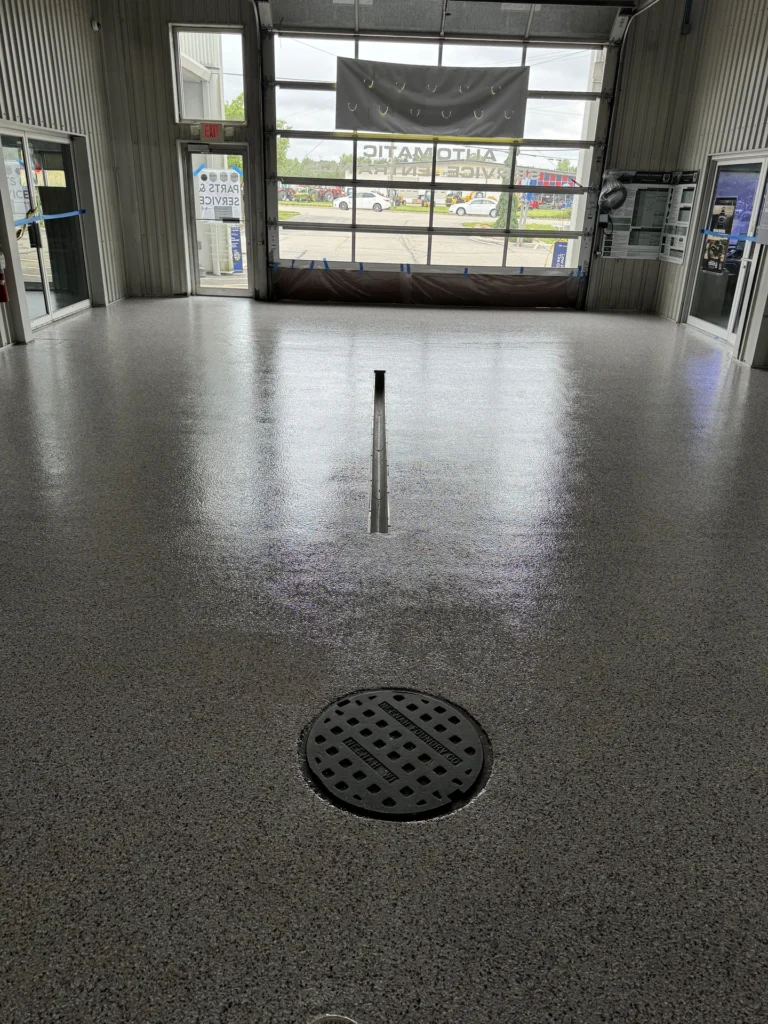 Metallic gray resinous floor coating with a decorative manhole cover drain in an automotive repair shop