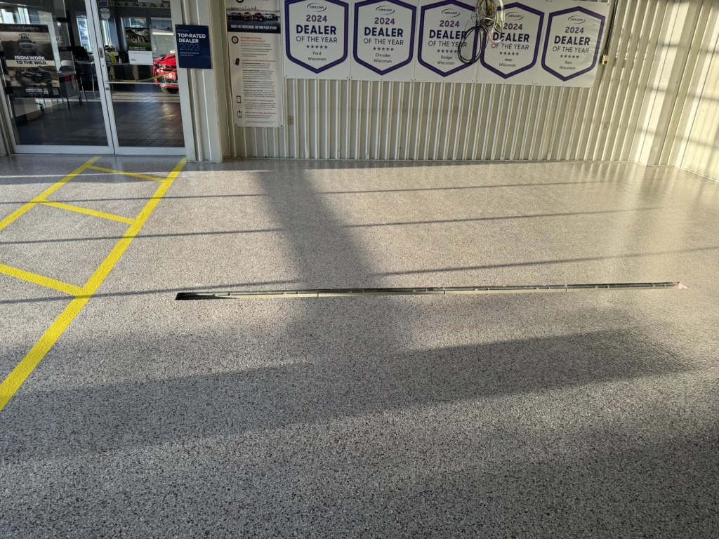 Smooth concrete floor with yellow markings leading to glass doors displaying car dealership awards
