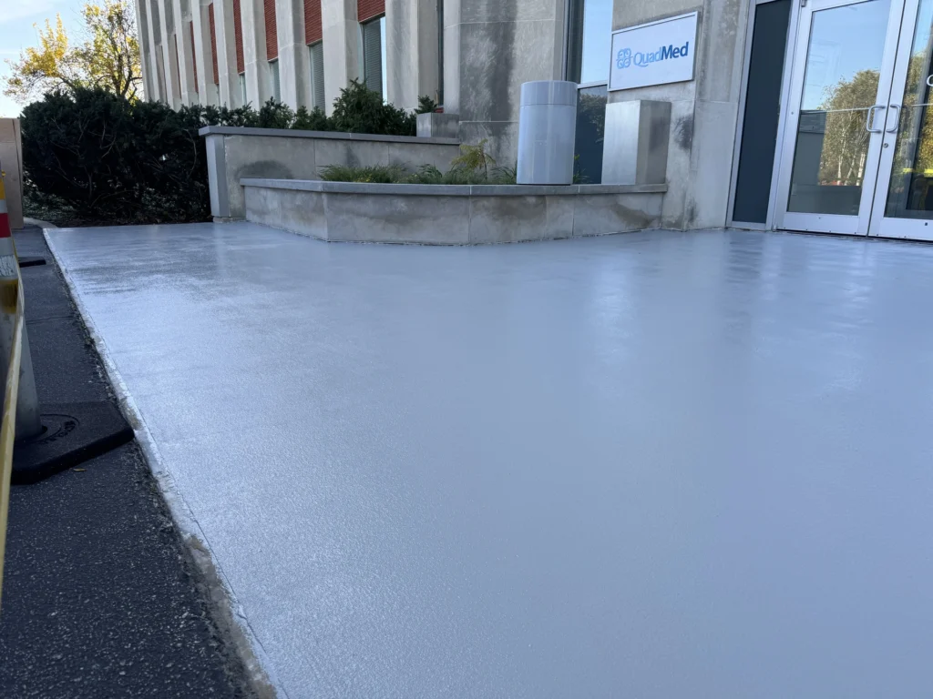 Smooth, light gray concrete floor coating outside a commercial building with glass doors and a QuadMed sign.