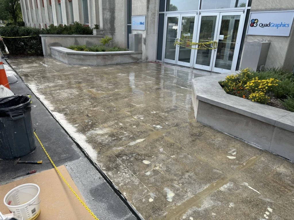 Concrete outdoor floor at commercial building entrance with caution tape marking off a repair area