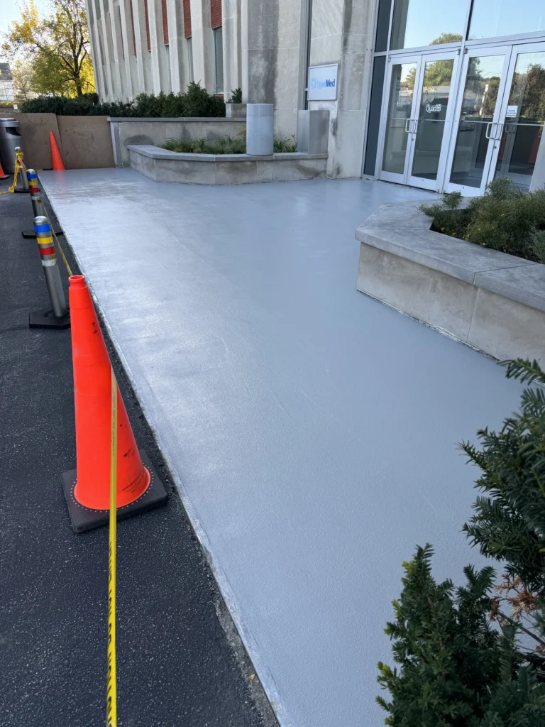 Smooth concrete flooring outside a commercial building with orange safety cones and plants nearby