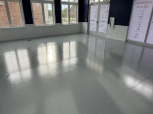Smooth, reflective commercial floor coating in an empty room with large windows and doors, showing a high-gloss finish