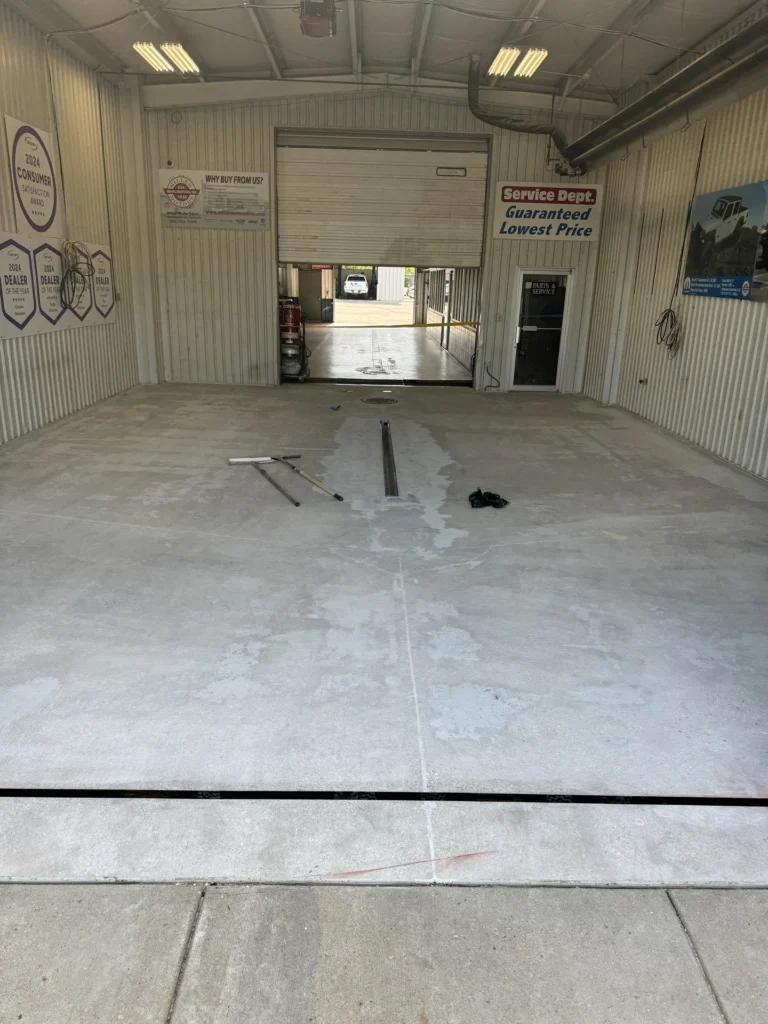 Empty commercial garage with concrete floor before floor coating installation, showing signs and tools on the ground