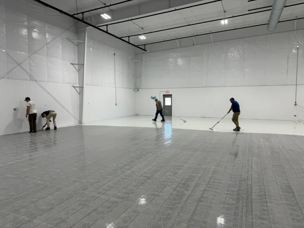 Workers installing a durable gray floor coating in a large commercial or industrial space with white walls