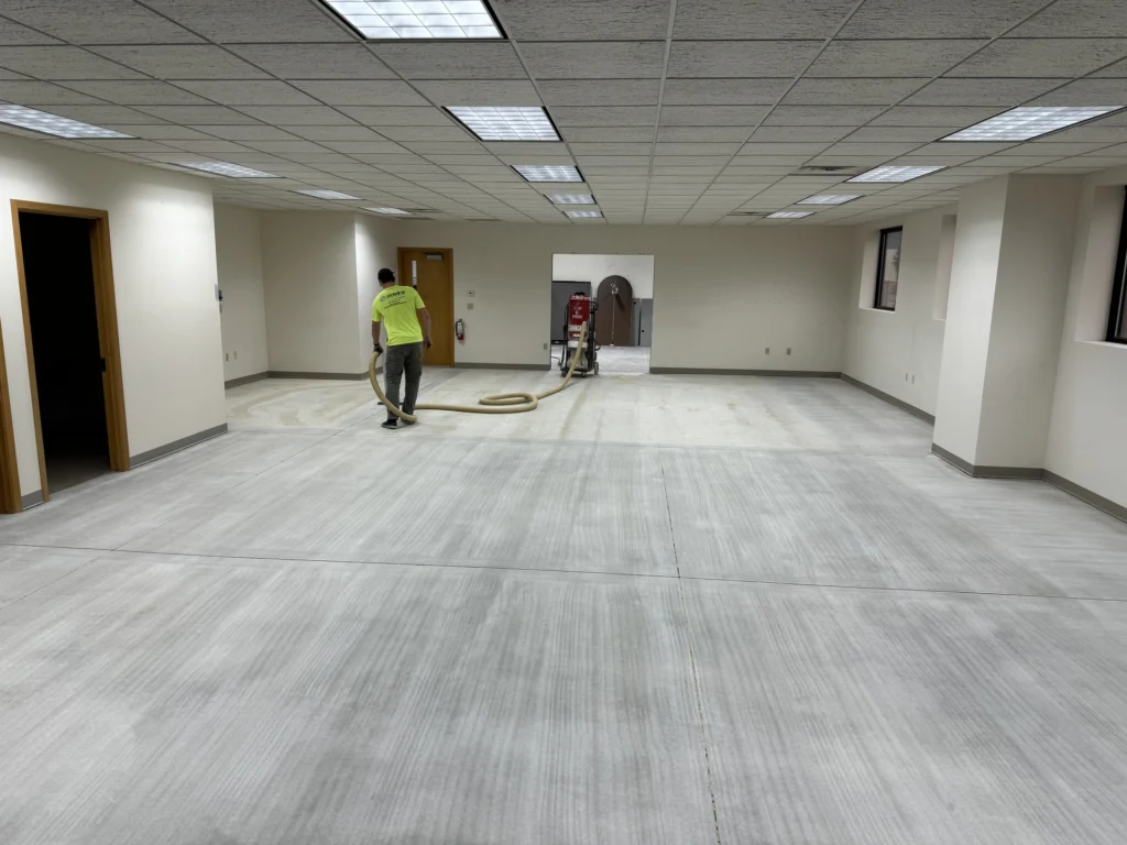 Workers installing gray flooring in a large commercial office space with drop ceiling and fluorescent lighting