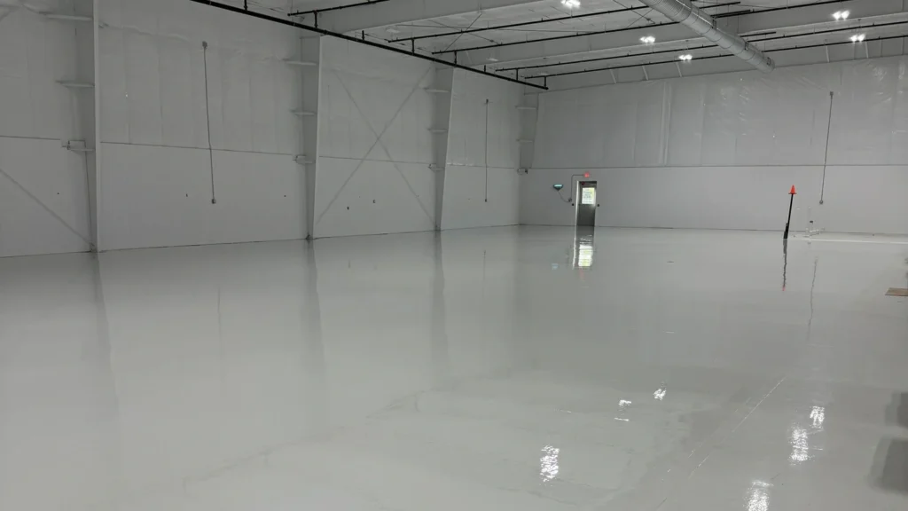 Spacious commercial warehouse or aircraft hangar like interior with smooth, reflective white epoxy floor coating and exposed ceiling