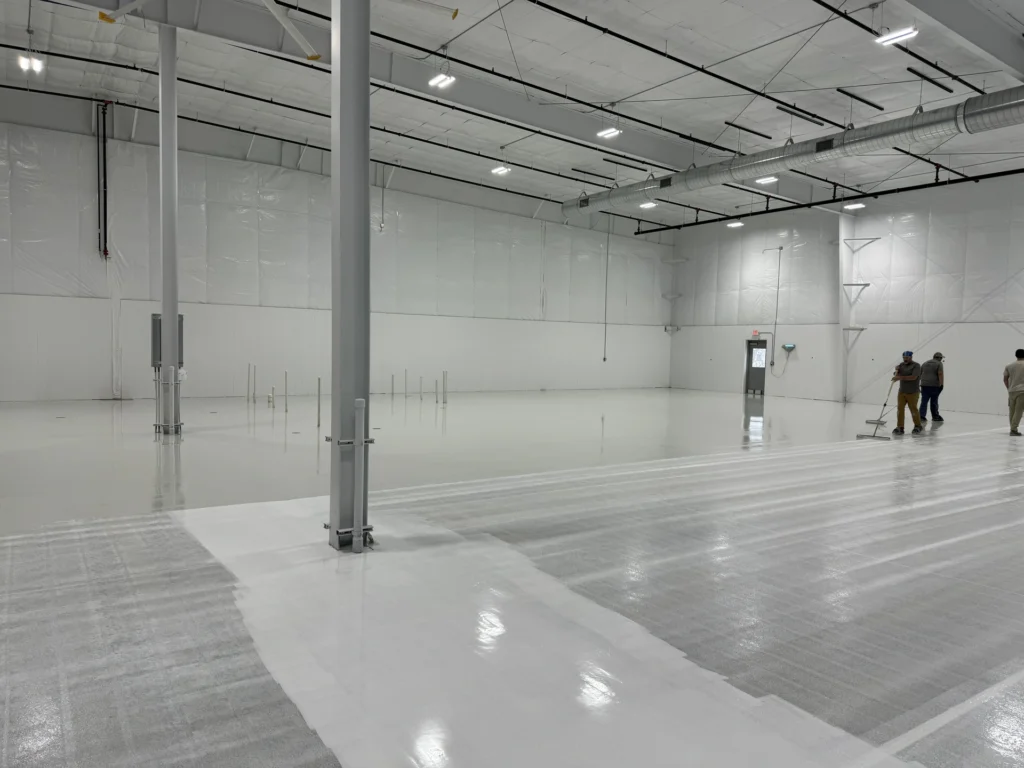 Spacious commercial warehouse interior with glossy gray epoxy floor coating, multiple workers visible