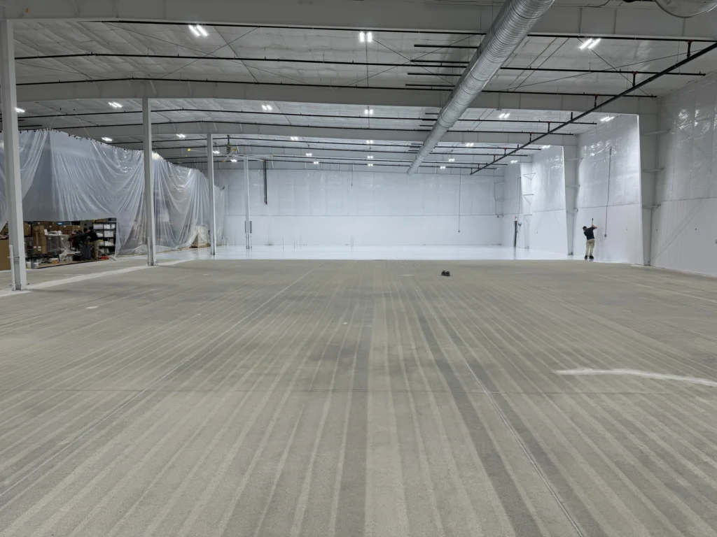 Spacious warehouse interior with light gray coated concrete flooring, white walls, and bright lighting