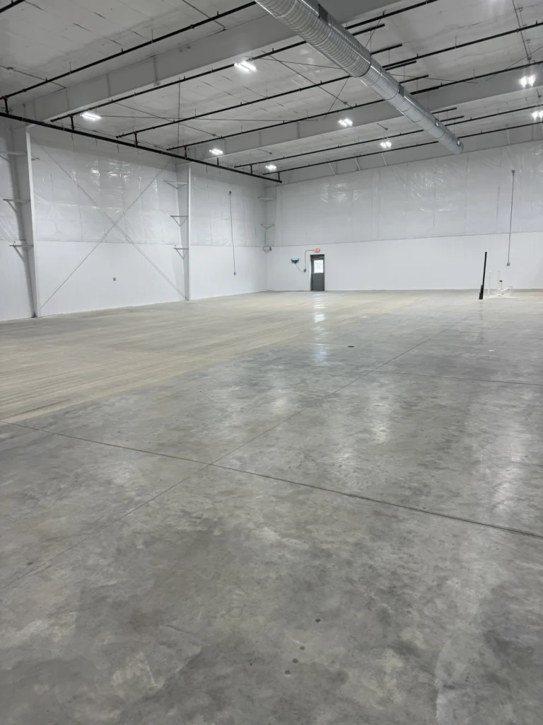 Empty commercial warehouse interior with polished concrete floor, white walls, and exposed ceiling beams and lighting