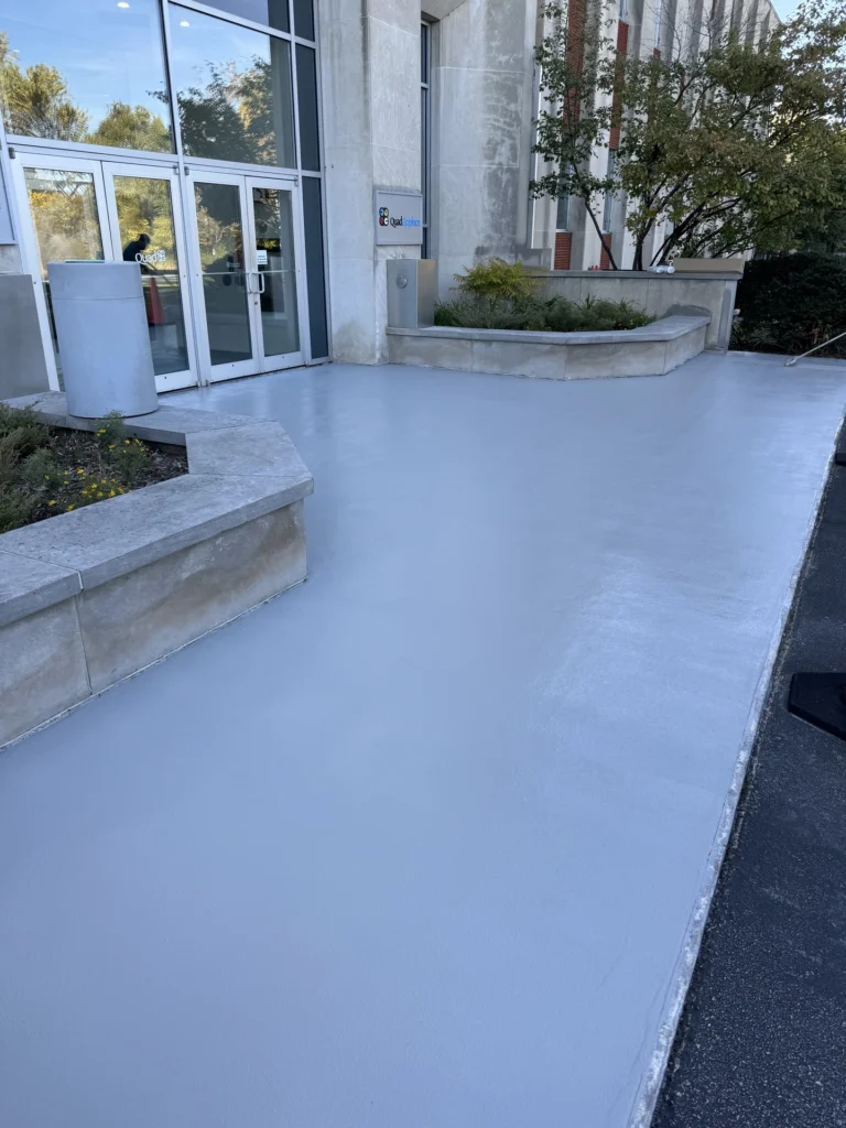 Smooth grey concrete coating applied to the entrance area of a commercial building with glass doors and windows