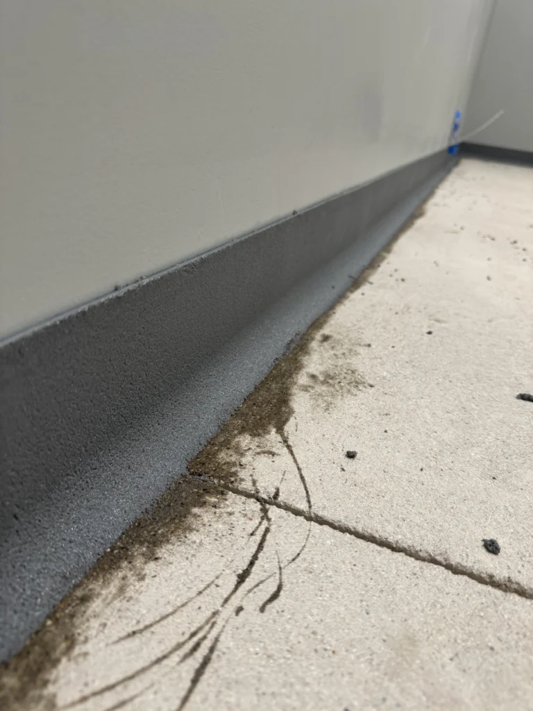 Close-up of a gray concrete floor with a dark gray cove base installed along the wall edge