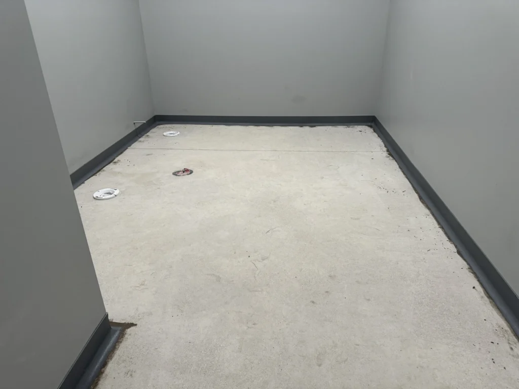 Partially installed metallic cove base on concrete floor, with exposed anchors and unfinished transitions