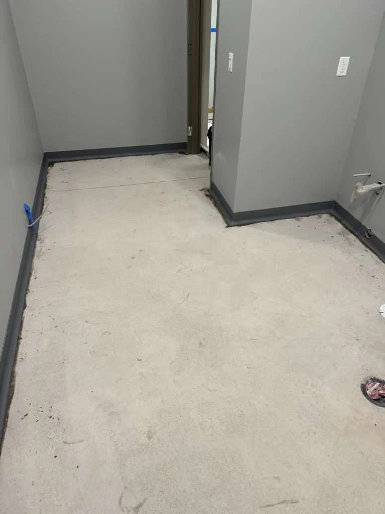 Bare concrete floor with dark cove base trim, prepared for coating application in a commercial or industrial space