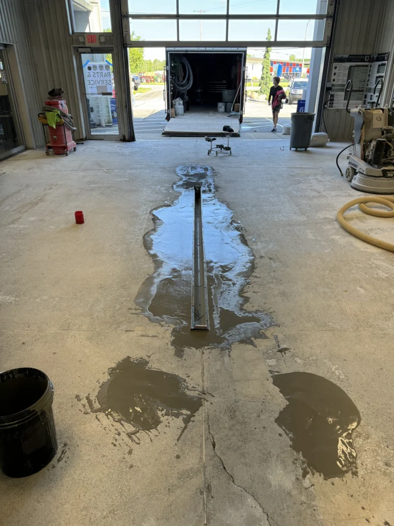 Concrete floor with a newly installed trench drain system surrounded by puddles of water in a commercial garage setting