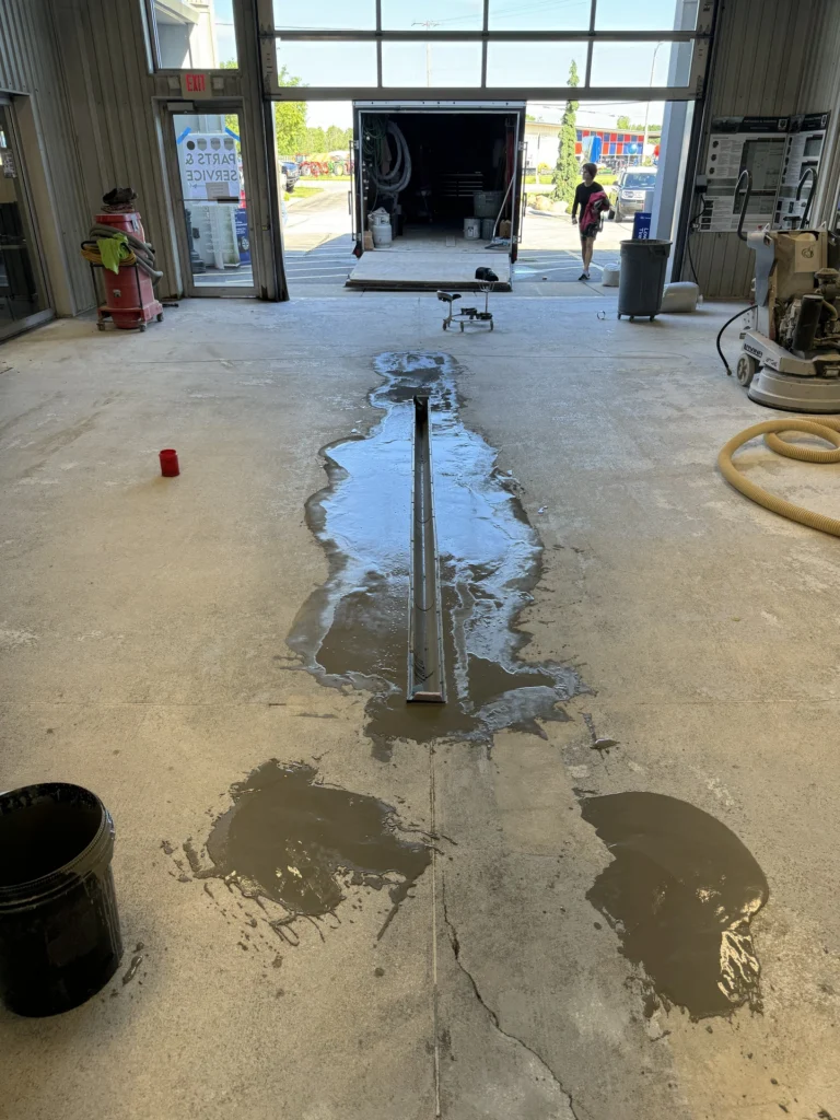 Wet concrete floor in a commercial building with water pooling, showing damaged areas that need repair