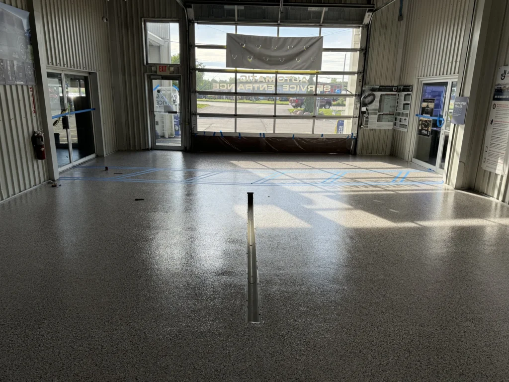 Shiny grey epoxy floor coating with blue tape lines in an auto repair shop with glass windows and doors