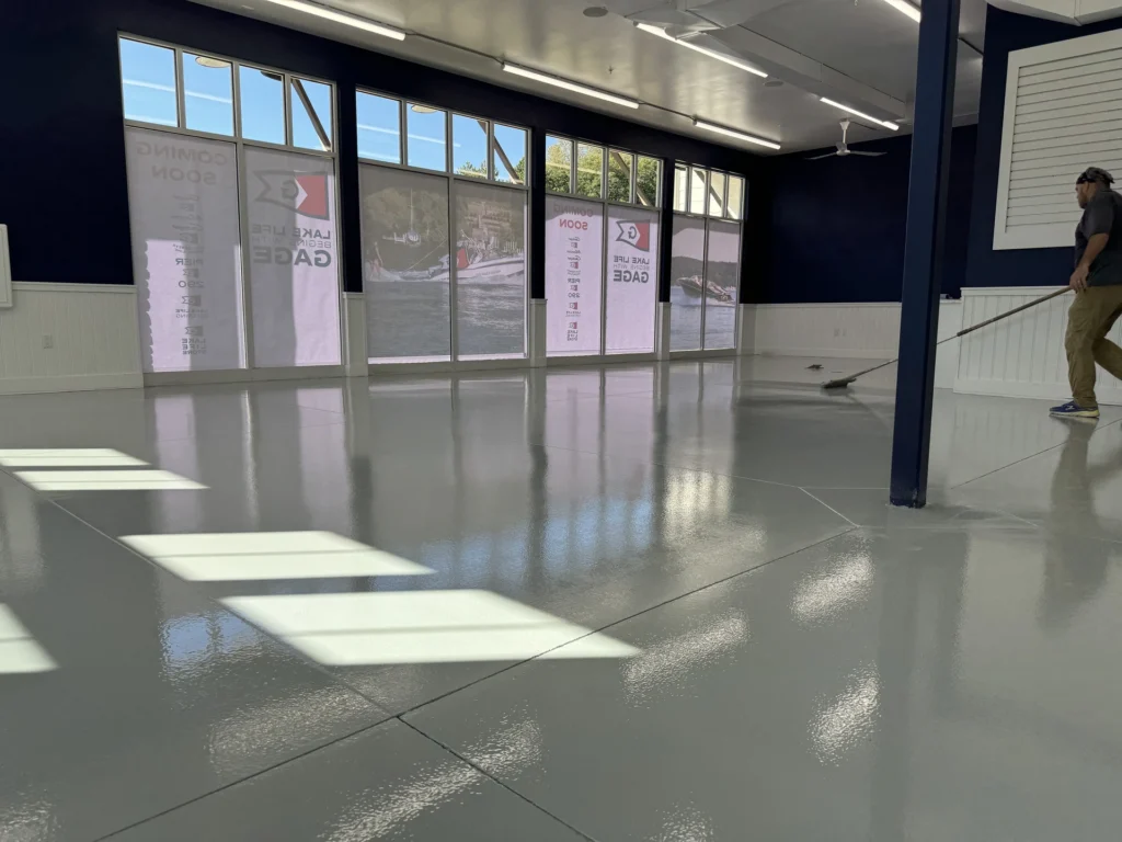 Shiny gray epoxy floor coating in a large empty commercial space with windows and sunlight reflecting off the surface