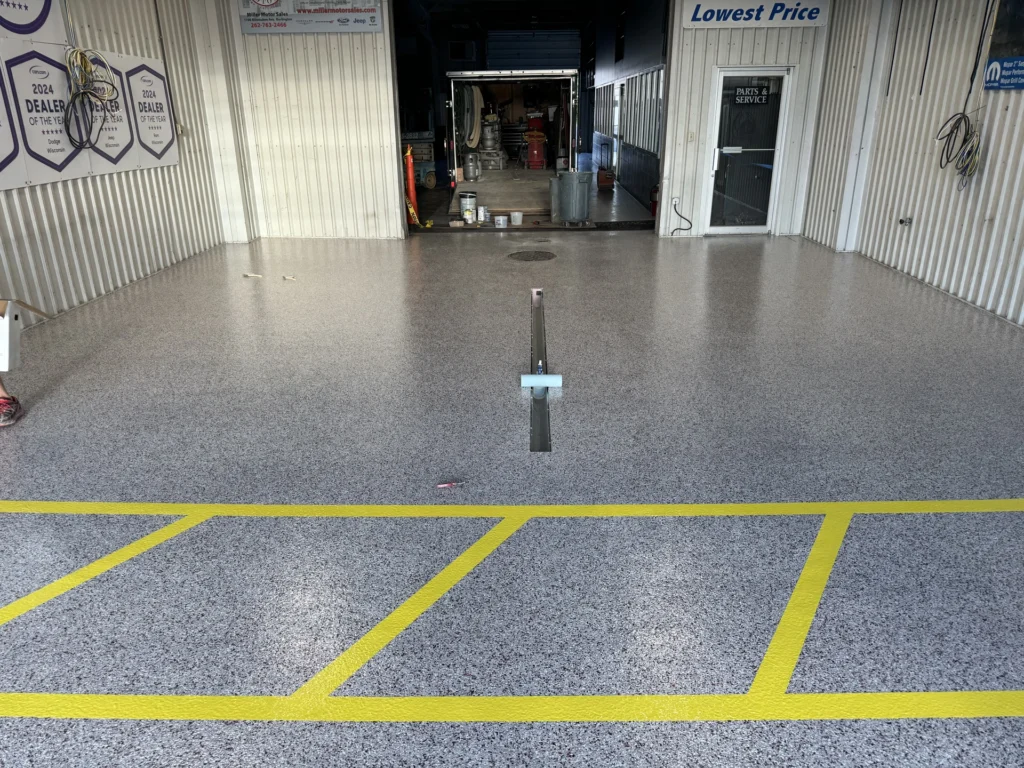 Epoxy garage floor with yellow striping and grey textured finish with various tools and equipment visible in the background