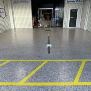 Epoxy garage floor with yellow striping and grey textured finish with various tools and equipment visible in the background