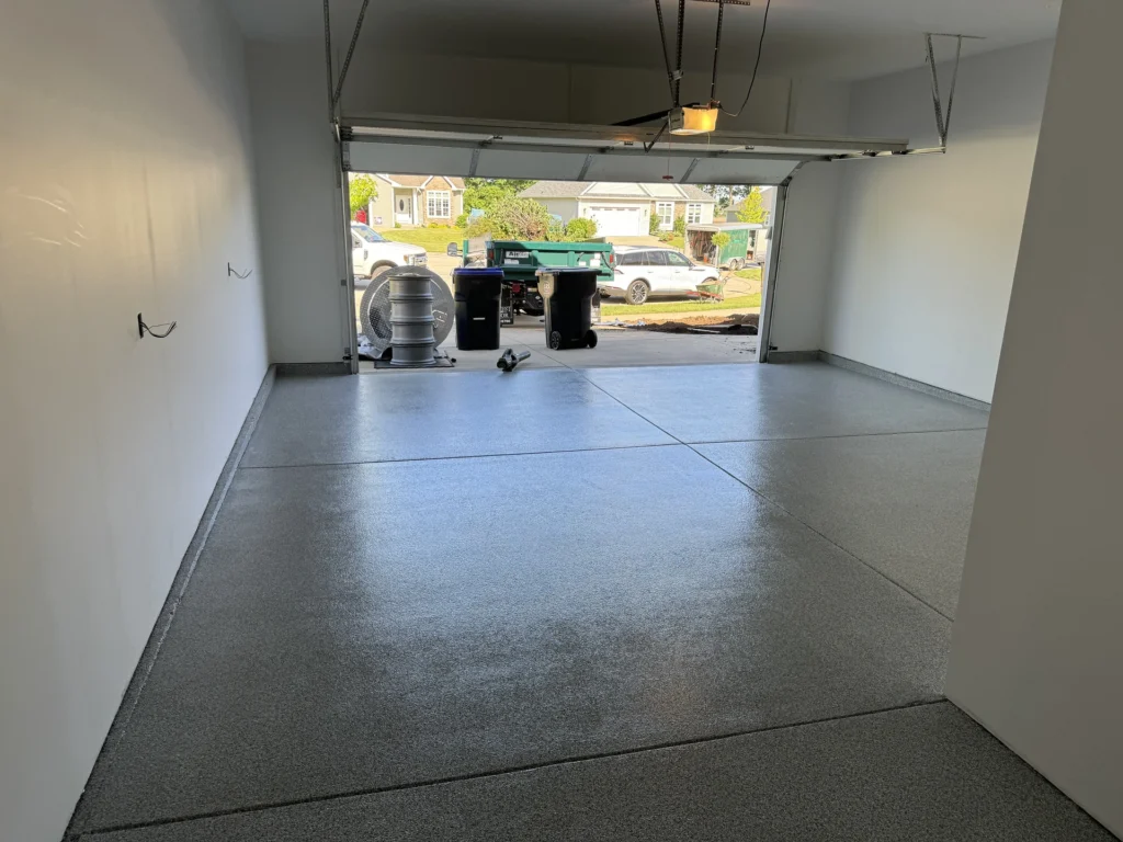Garage interior with newly installed grey floor coating, equipment, and view of residential neighborhood outside