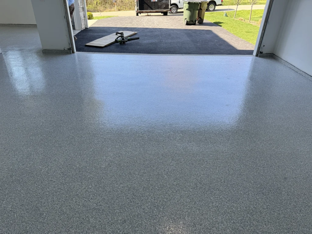 Smooth gray concrete floor coating in a residential garage with tools and a vehicle visible in the background
