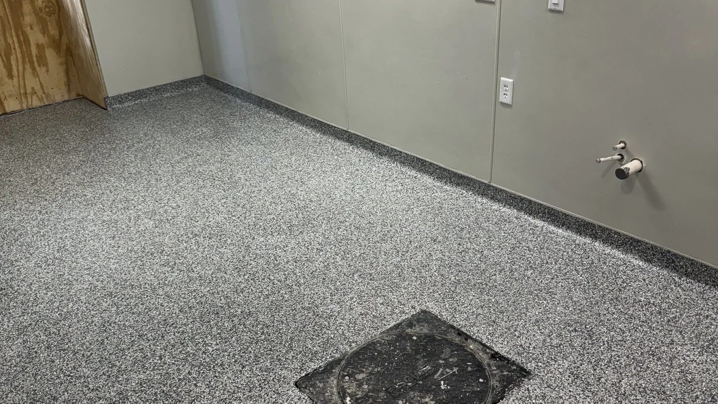 Gray flake epoxy flooring with a square drain and gray walls in a commercial or industrial setting. May be a hospitals treatment room