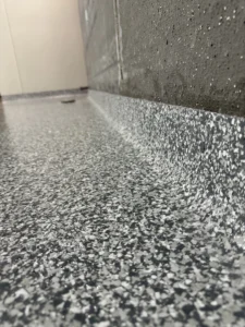 Close-up view of a textured, speckled gray industrial epoxy flooring surface with water droplets