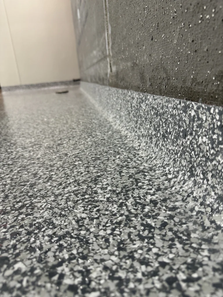 Close-up view of a textured, speckled gray industrial epoxy flooring surface with water droplets