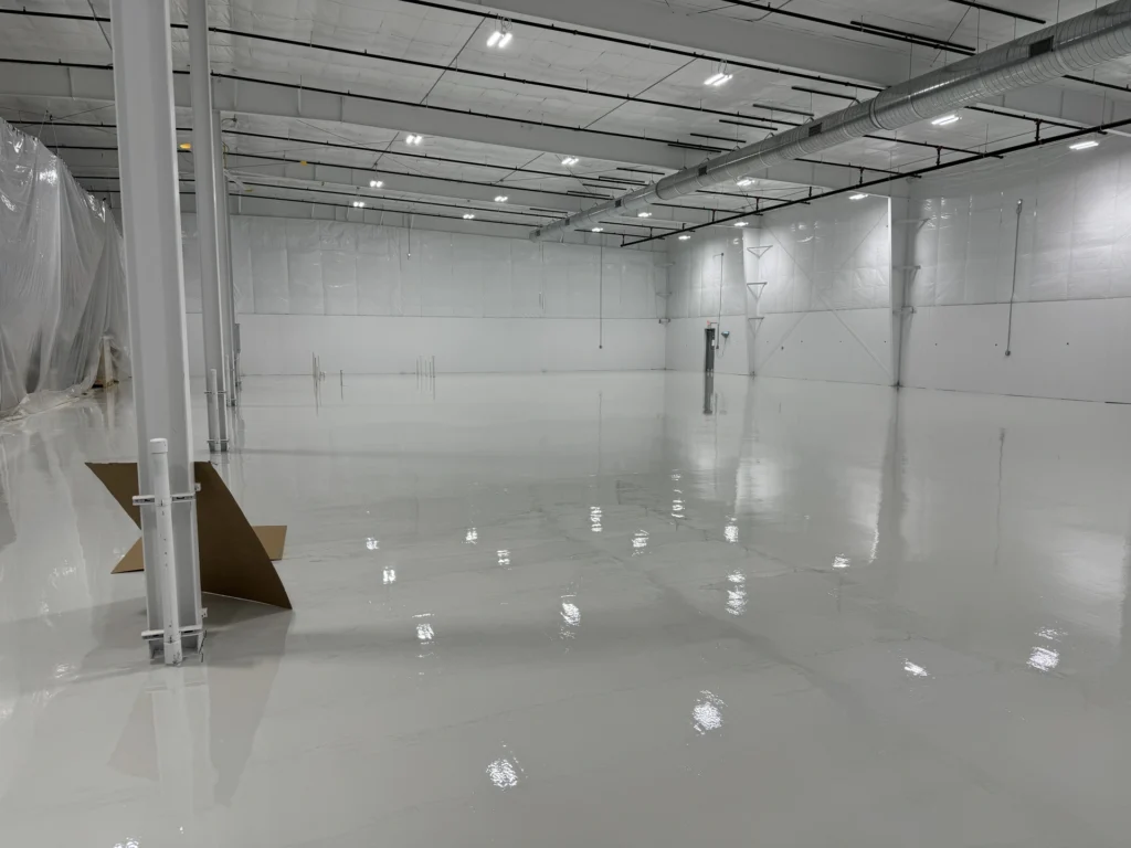 Large empty industrial facility interior with smooth reflective epoxy floor coating and covered equipment