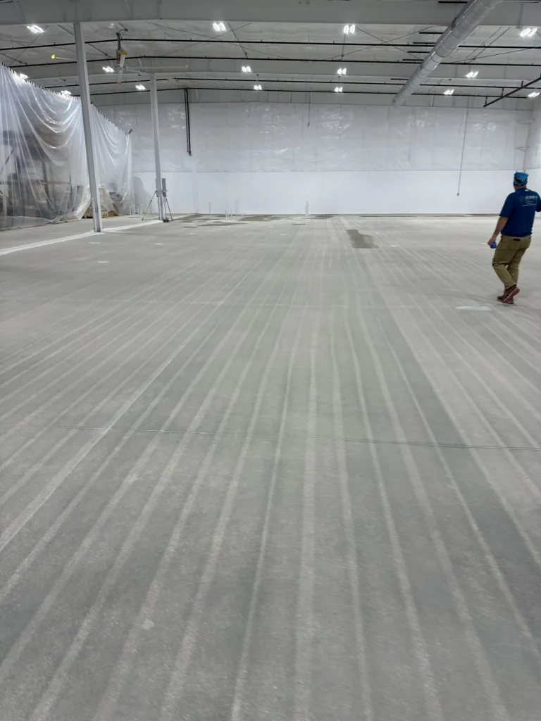 Worker inspecting a large, empty industrial warehouse with a pristine light gray epoxy floor coating.