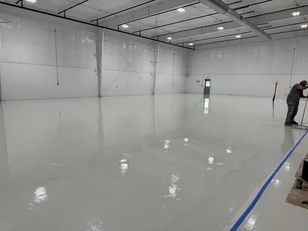 Large industrial warehouse with a high-gloss, light gray epoxy floor coating, reflecting ceiling lights