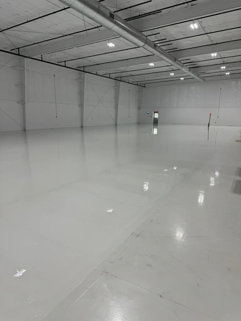 Bright white epoxy floor coating in a large industrial warehouse with exposed ductwork and ceiling