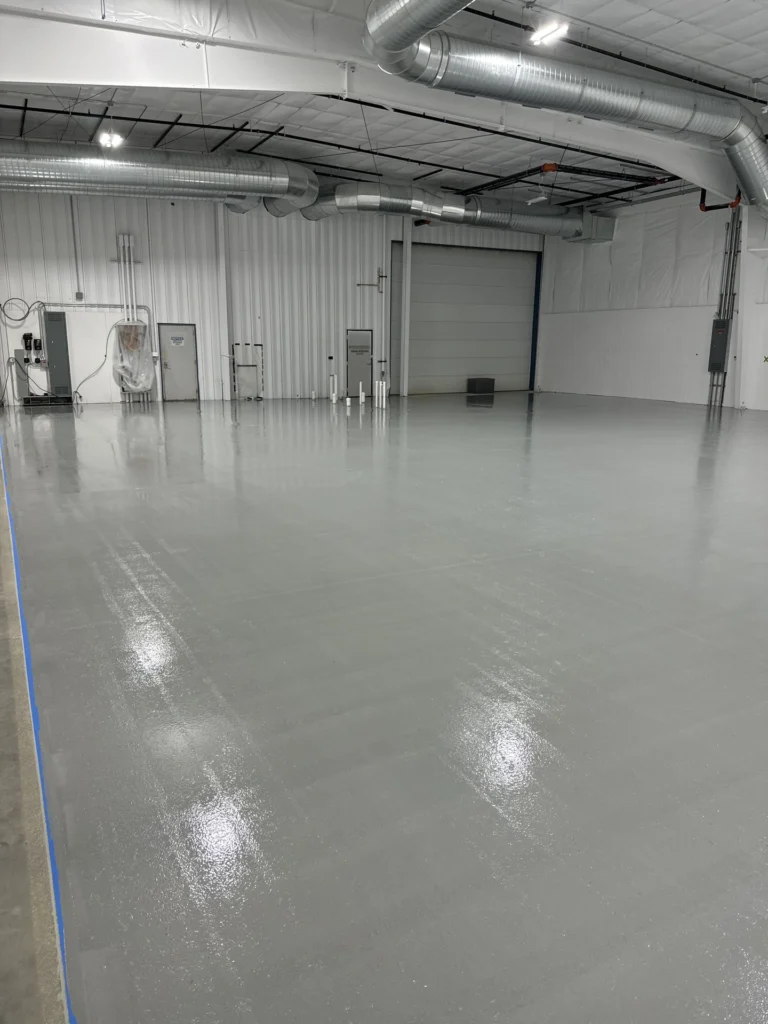 Expansive industrial warehouse interior with smooth, reflective gray epoxy floor coating and exposed ductwork overhead