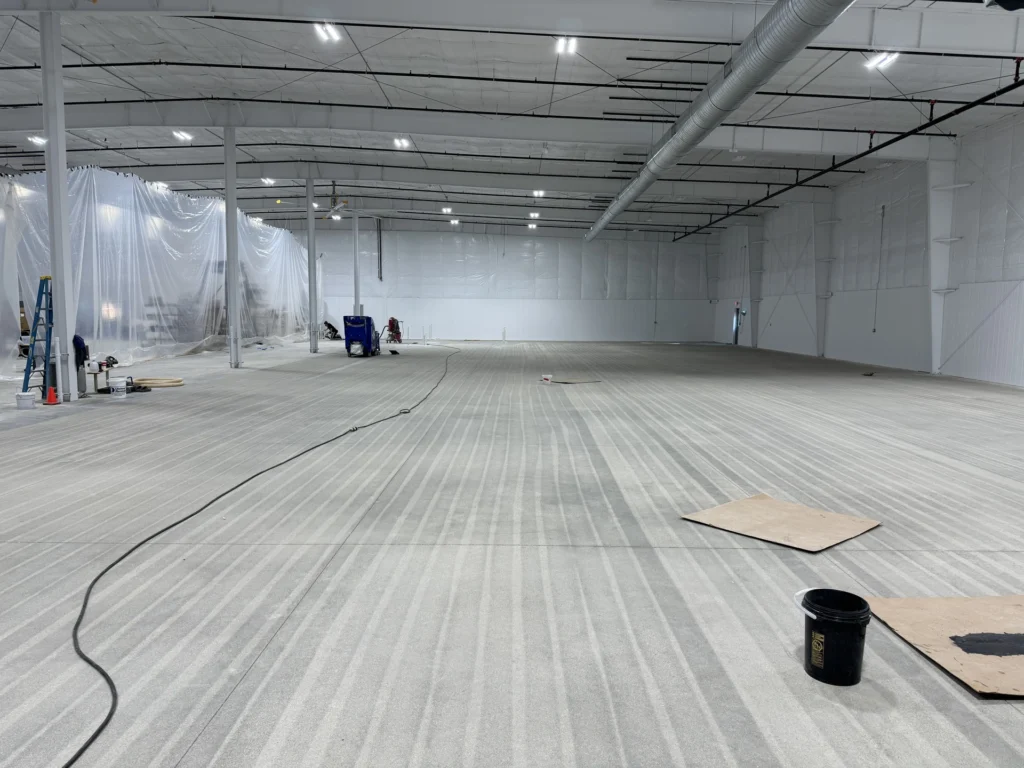 Large industrial warehouse interior with light gray resinous floor coating being installed by workers