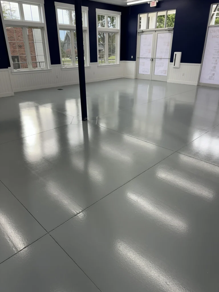 Industrial interior space with light gray reflective floor coating, large windows, and doors along the walls
