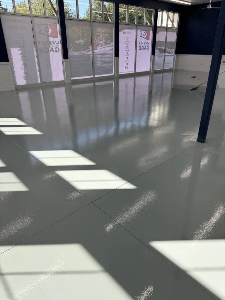 Polished gray concrete floor with square patterns of sunlight in a modern office lobby with glass walls