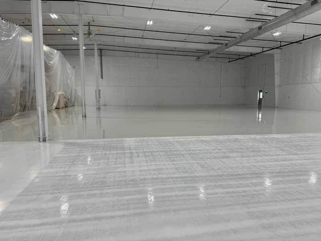 Spacious warehouse interior with smooth, glossy gray epoxy floor coating, reflecting overhead lighting.